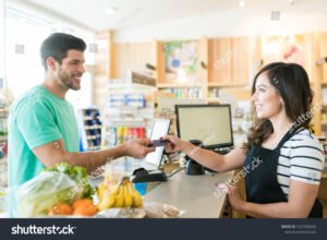 hymyileva asiakaspalvelija kassalla auttamassa ostajaa