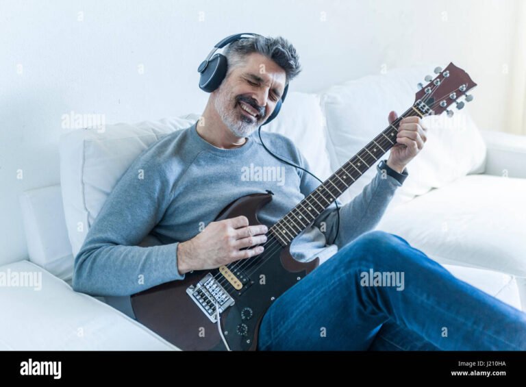 ihminen soittaa kitaraa kotona kuulokkeet paassa
